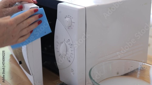 Person is cleaning a microwave with a blue cloth. The microwave is white and has a black door
