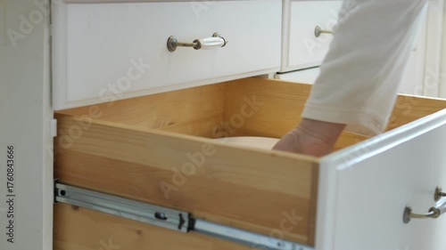 Person is reaching into a white dresser drawer. The drawer is open and has a silver drawer pull
