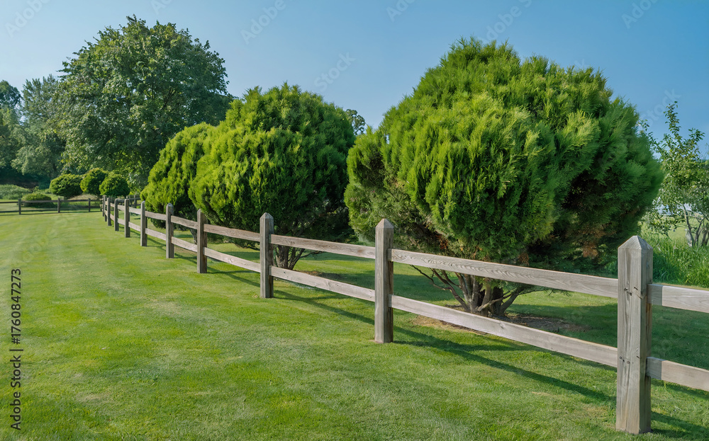 Fototapeta premium A Wooden Rail Fence in a Beautifully Landscaped Garden, Bordering a Manicured Green Lawn and Lush Shrubs on a Sunny Summer Day