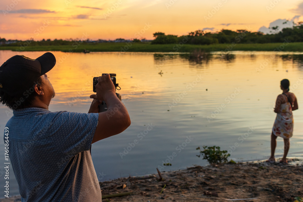 Obraz premium Person taking photos of the Amazon sunset with their cellphone, as the sky glows over the rainy jungle of Peru