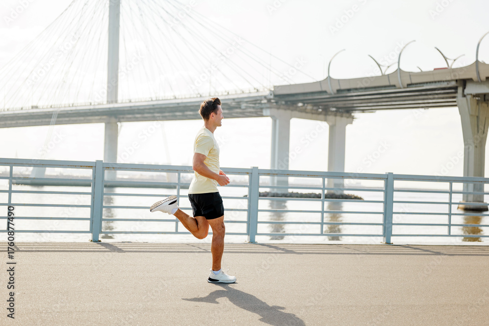 Fototapeta premium Man running along waterfront path near bridge during morning exercise routine in urban setting