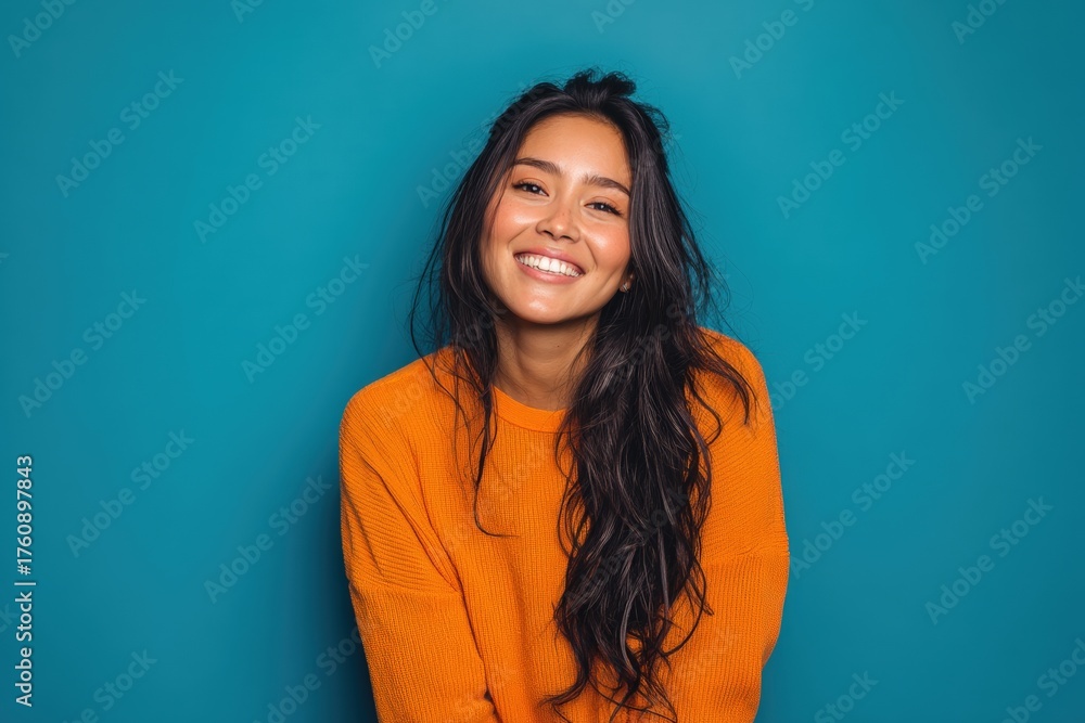 Fototapeta premium Smiling person with long dark hair wearing an orange sweater, looking cheerful. The vibrant image captures warmth and joy. The scene is bright and uplifting, creating a positive vibe