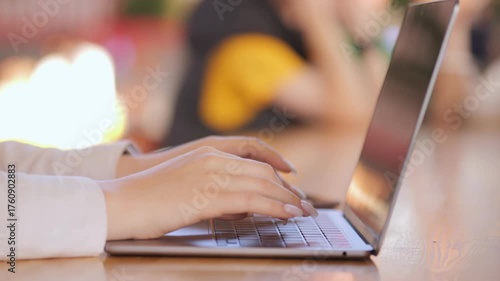 Woman is typing on a laptop. The laptop is open and the screen is black. The woman is wearing a white shirt