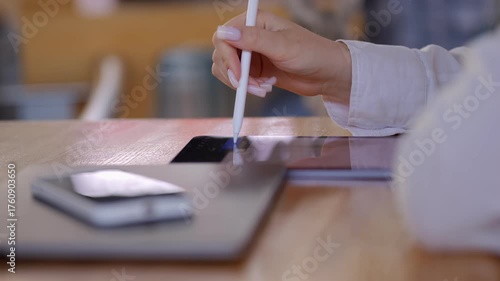 Person is writing on a tablet with a pen. A cell phone is on the table next to the tablet