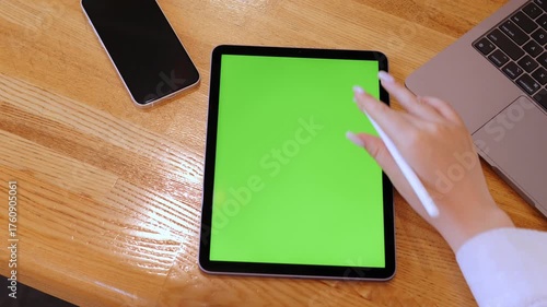 Person is using a tablet with a green screen. A white cell phone is on the table next to the tablet