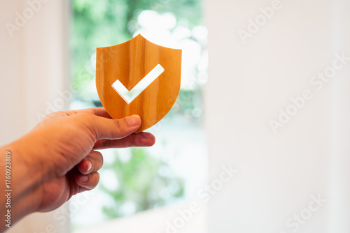 Foto Hand holding wooden shield with check mark symbol on blurred background