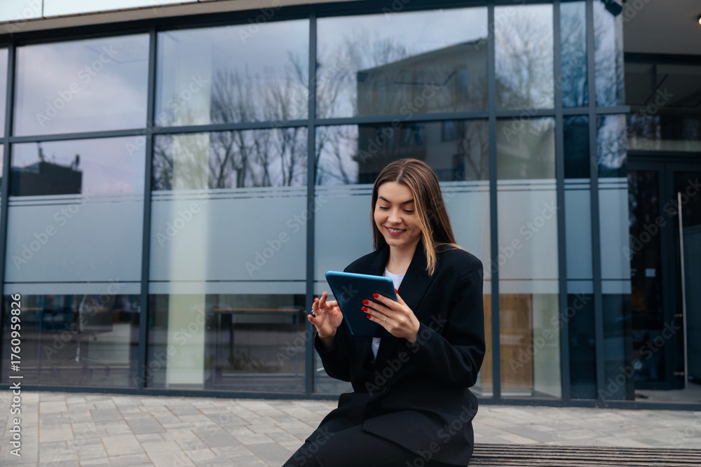 Fototapeta premium Young Woman Using Tablet Outside a Modern Building During a Cloudy Day While Enjoying Her Time and Smiling