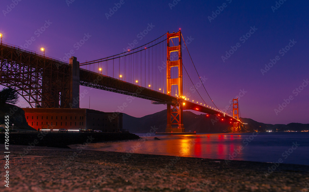 Obraz premium Golden Gate Bridge architectural landmark in San Francisco, California, USA, illuminated at night with reflections on the bay water, suspension bridge design, engineering structure, travel destination