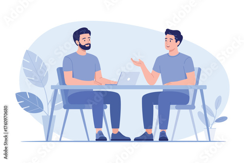 Two men in blue t-shirts talking and gesturing while sitting at a table discussing ideas collaboratively