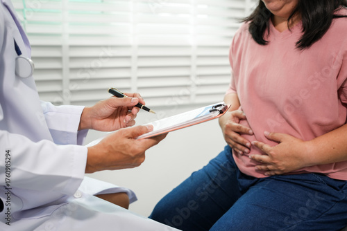 Obraz na plátně The doctor will take a medical history and assess the Asian woman's abdominal pain and discuss diagnosis and management of gastrointestinal problems, excess fat, obesity, or other health problems