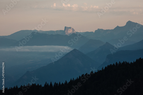 Paysage de montagne au coucher du soleil, avec des couches successives de reliefs bleutés, de brume et de forêts sombres. Image apaisante et atmosphérique, parfaite pour des projets liés à la nature, 