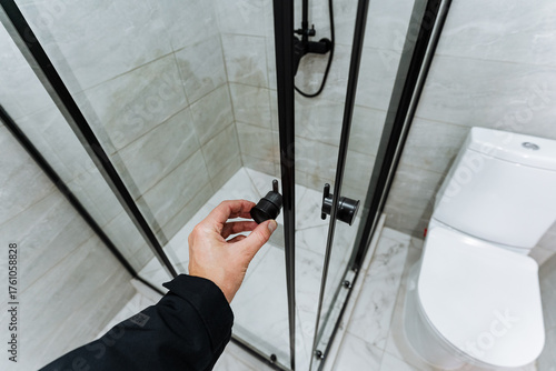 fixing shower door hinge, professional plumbing and door maintenance, worker skillfully adjusting shower door hinge near toilet with specialized tools and attention to detail