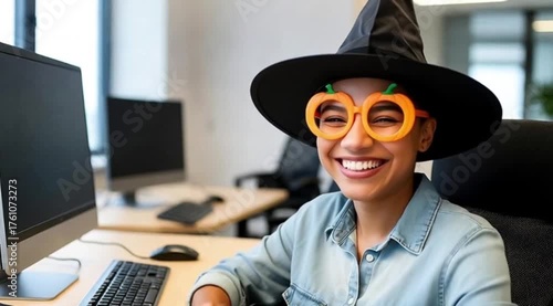 Cheerful Office Woman in Witch Hat and Pumpkin Glasses Smiling and Waving Playfully – Halloween Celebration.