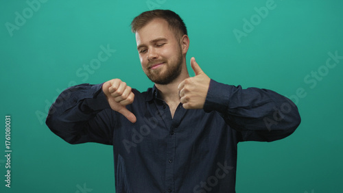 Foto Young caucasian man showing thumbs up and thumbs down in studio against a teal backdrop with closed eyes and a subtle smile; ambivalence choice