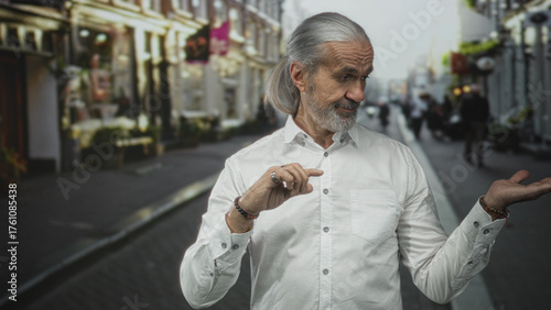 Man points finger with right hand and shows open left palm while standing on a busy city street in daylight, wearing white shirt; subtle confidence wisdom.