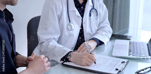 Doctor and patient are talking in clinic after usual health check up. Female physician is making notes awhile man is describing something. Medicine concept