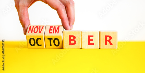 Symbol for the change from October to November. Businessman turns wooden cubes and changes the word October to November. Beautiful white and yellow background. Happy November concept. Copy space.