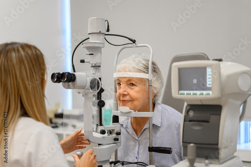 Female ophthalmologist performing eye exam on senior woman with slit lamp during vision assessment at clinic