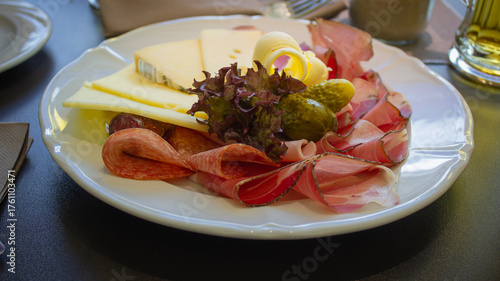 Rustic charcuterie platter with cured meats, cheeses, and pickles served with beer in alpine setting. San Candido, Italy