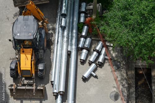 Excavator and metal pipes at construction site from above