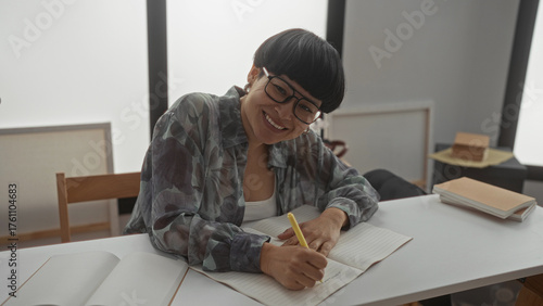 Woman writing in a notebook happily in a modern living room filled with books, showcasing a cozy and educational atmosphere.
