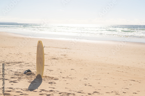 Yellow surfboard standing in sand on Atlantic beach. Caparica, Lisbon, Portugal. 2 December 2023.