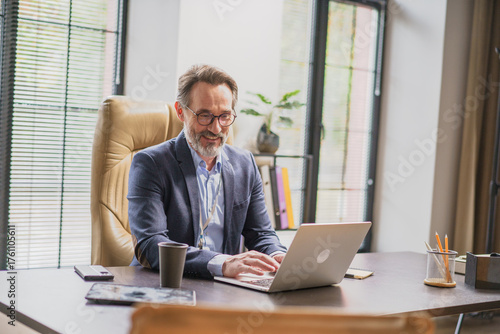 A dedicated professional man enjoys a productive workday at his stylish office desk, fully engaged with his laptop, exuding joy and concentration during his tasks