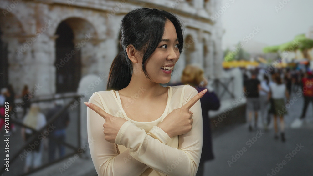 Fototapeta premium Young chinese woman smiling and pointing at both sides outside the roman coliseum, showcasing a lively outdoor scene in rome's iconic architecture.