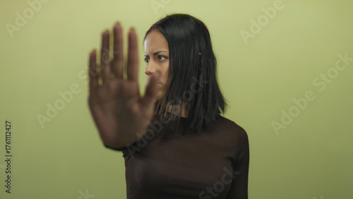 Woman gesturing stop with her hand against a yellow background, expressing firmness and seriousness in an isolated setting, emphasizing a message of rejection and boundary.