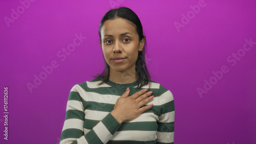 Tableau sur toile Young hispanic woman making pledge gesture against isolated pink background wall, wearing striped sweater, expressing serious commitment and solemn promise