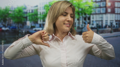 Bild auf Leinwand Blonde woman displays thumbs up and thumbs down on an amsterdam street by a canal; uncertainty conflict