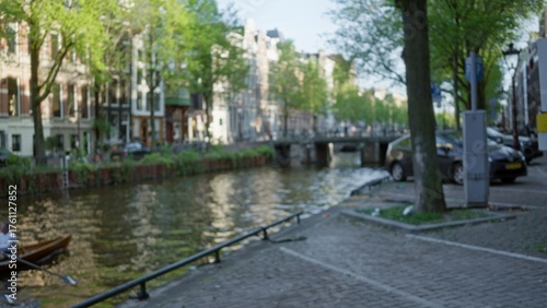 Photos Urban canal scene in amsterdam with blurred buildings and a man rowing in a bokeh backdrop under the greenery of the netherlands
