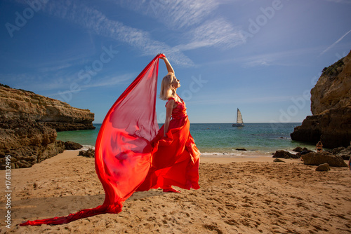 Woman in flowing red dress on ocean beach