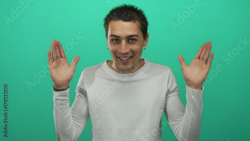 Vászonkép Young man wearing white shirt covers eyes with hands then lowers hands and smiles in studio; playful joy