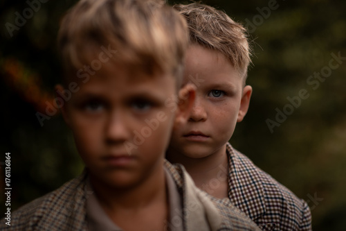 Close portrait of two serious boys, one standing behind the other. Focus on  eye, blurred front face. Concept of childhood, identity, and emotional connection.
