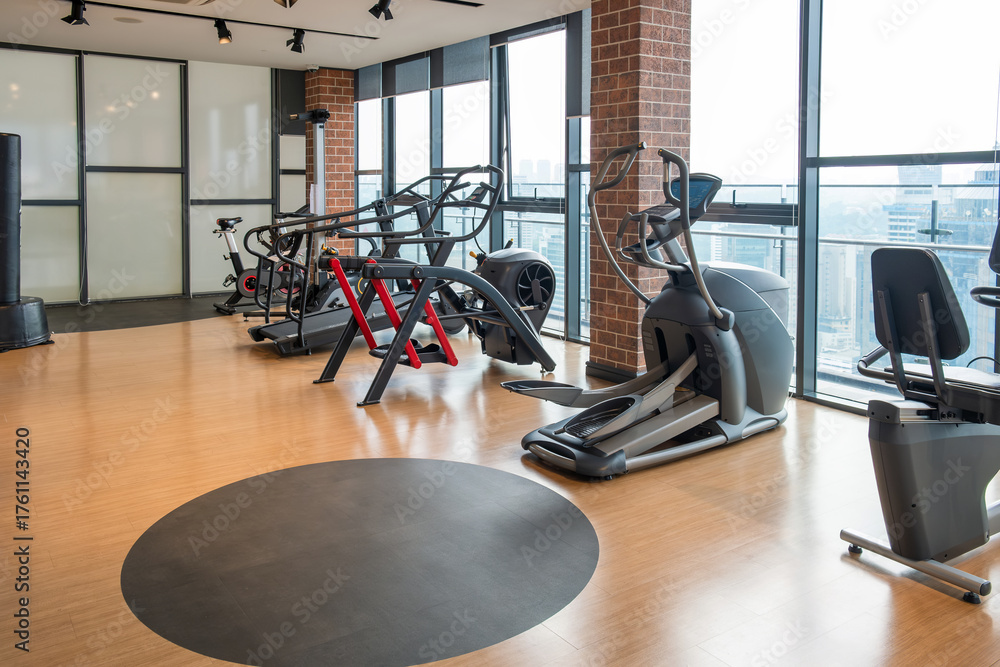 Obraz premium Modern gym interior with various fitness machines including elliptical trainers, treadmills and bikes and large windows with panoramic city view. Urban wellness, fitness, luxury, contemporary living