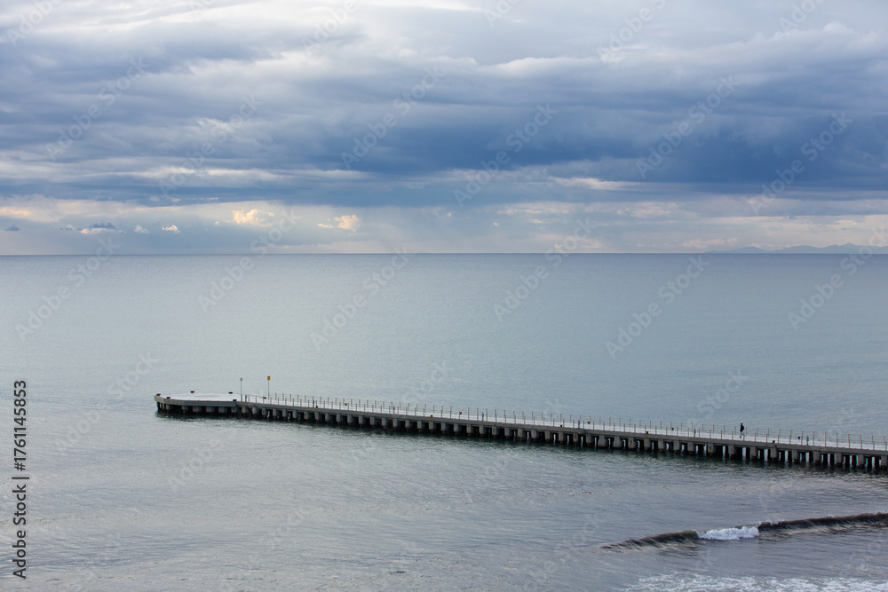 Fototapeta premium Gentle sunbeams pierce through a blanket of clouds, illuminating the calm sea and misty coastal mountains. The soft light creates a serene and ethereal atmosphere, highlighting the peaceful beauty