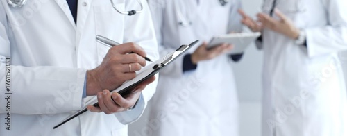 Doctor writing on a clipboard during a medical team discussion, collaborating on patient care, documentation, and healthcare strategy in a clinical setting
