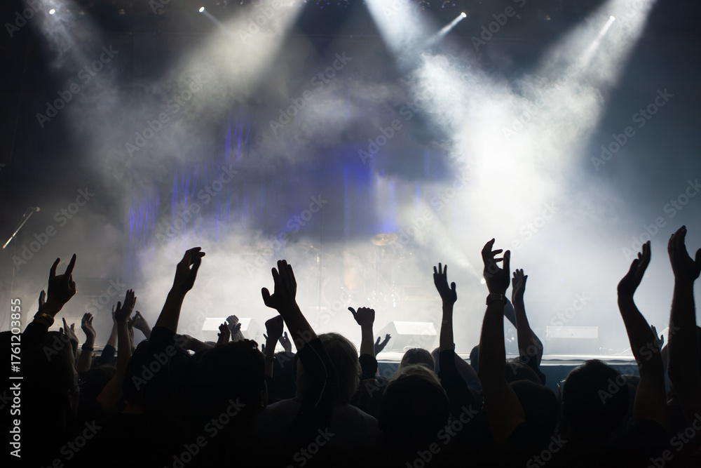 Fototapeta premium Concert audience raises hands, enjoying live music under bright stage lights and smoke effects. Entertainment industry, event organization, music performance.