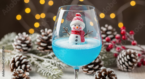 Festive winter cocktail with a cute snowman decoration in a wine glass. Creative blue Christmas drink with bokeh lights.
