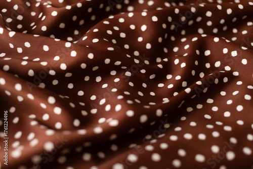 Close-up of terracotta colored silk fabric with white polka dots, softly draped to create an abstract background. Copy space