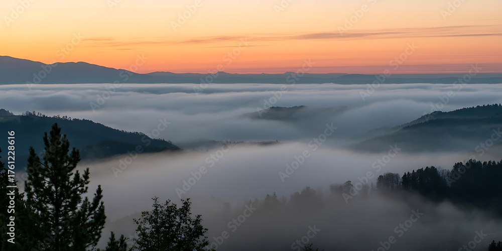 Fototapeta premium Mist-filled valley nestled between mountains, bathed in the warm hues of a stunning sunrise.