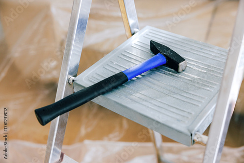 Black and blue hammer resting on aluminum step ladder in a construction