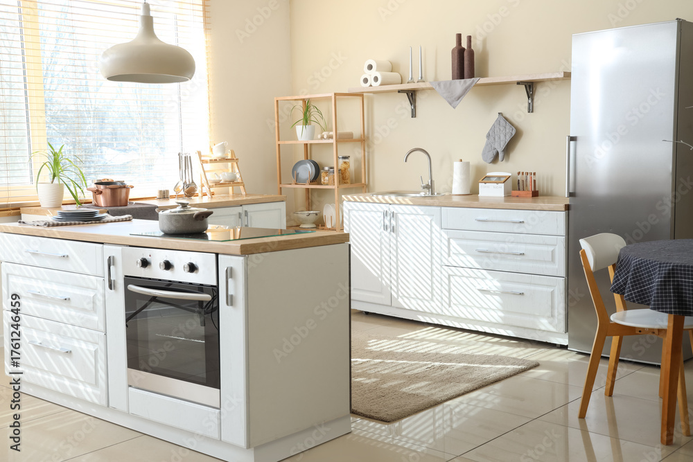 Fototapeta premium White counters and silver fridge near beige wall in interior of kitchen