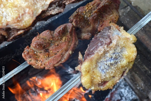 Traditional southern Brazilian barbecue being prepared the old fashioned way, with iron stick and outdoors. Seasoned pork and rump steak.