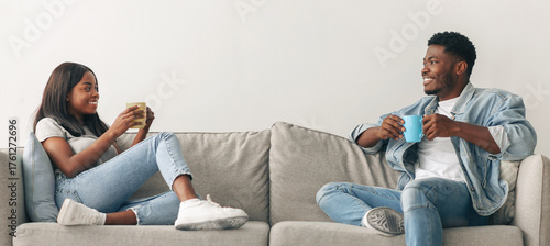 Stay At Home Date. Beautiful African American couple drinking coffee and talking, resting on the couch indoors at home in living room, relaxing enjoying company of each other spending weekend together