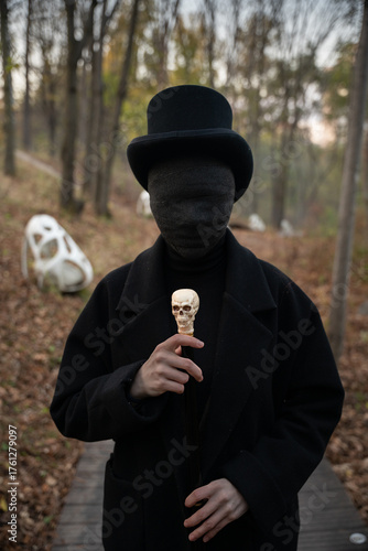 A man with a face in black bandages is dressed in an old vintage style: a classic black coat and tweed vest, a top hat, a walking stick with a skull in his hands. The invisible man or the zombie