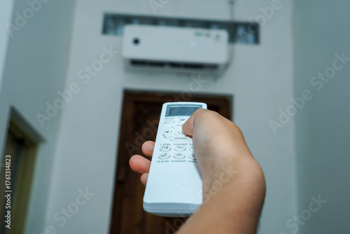 view of a hand holding the AC remote control with the AC mounted on the wall.