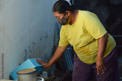 A mother puts down the blue feed container beside the wall of her house after completing chicken feeding duties.