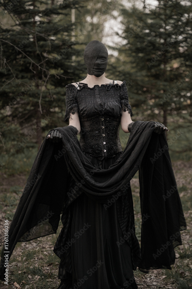 Naklejka premium A creepy monster or the ghost of a witch woman with blackened hands and a face wrapped in black bandages in an antique dress with a corset. The Forest witch or the spirit
